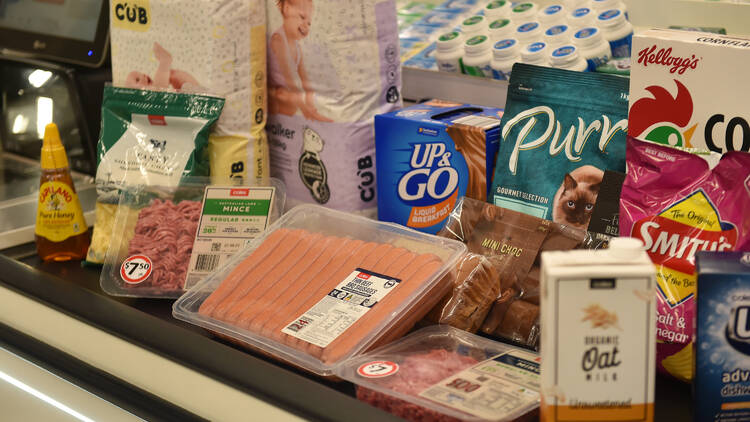 A supermarket check-out lane with products like sausages, cereal, milk and nappies.