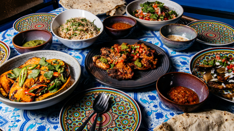 A spread of Afghan food in assorted bowls sits on a blue tiled table
