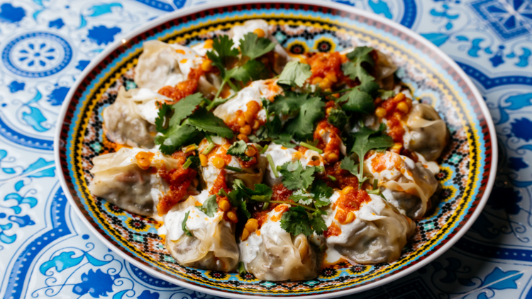 A round plate covered in Afghani dumplings covered in red sauce and green herbs