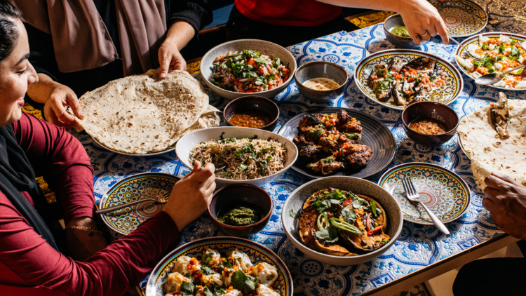 A group of Afghan women sit around a table covered in multiple dishes at Kabul Social