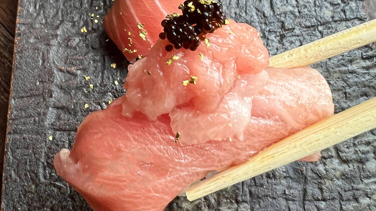 A pair of chopsticks holding a piece of tuna nigiri topped with caviar.