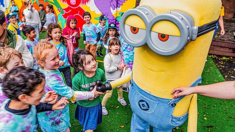 Kids are shaking hands with a giant yellow minion