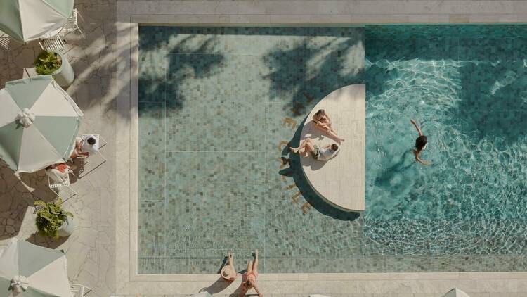 A beautiful swimming pool surrounded by marble flooring and white shade umbrellas 