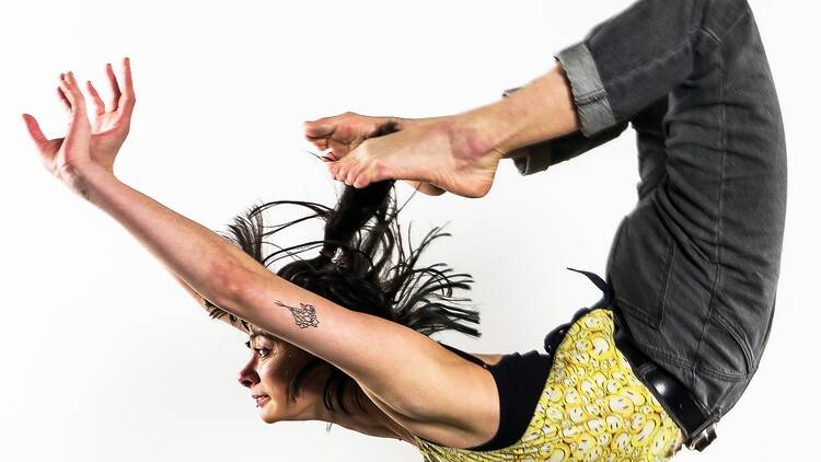 A woman performs a circus act in the air with her arms up and legs behind her back