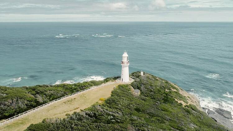 A white lighthouse at the edge of a cliff overlooking the ocean.