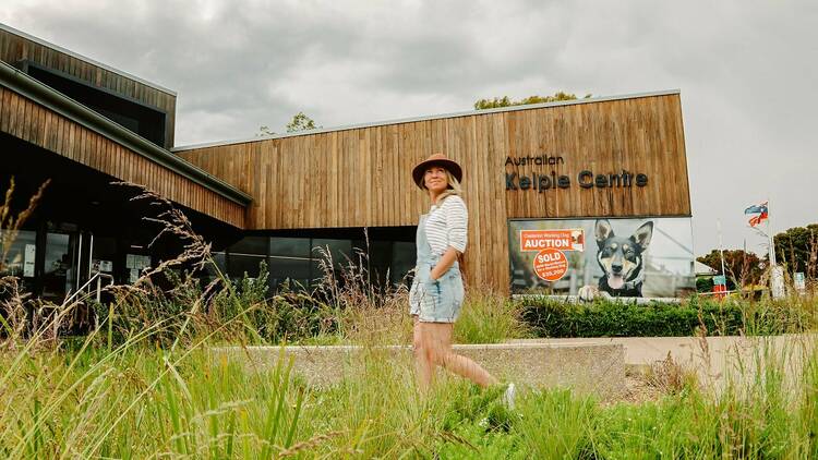 A blonde woman in overalls and a hat walks past the Australian Kelpie Centre.