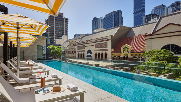 A photo of the pool area at Hyatt Regency which contains a long, anrrow pool, and lounge chairs with white, yellow striped outdoor umbrellas and the cities buildings in view