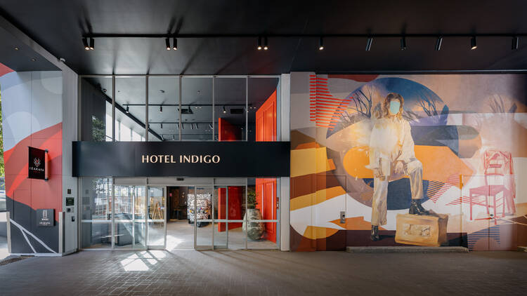 The exterior of Hotel Indigo with a  mural of a woman with her foot on a crate 