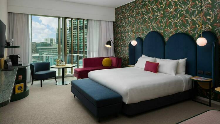 A photo of a room containing a blue fabric bed and headboard, with white sheets and a hot pink pillow and matching couch