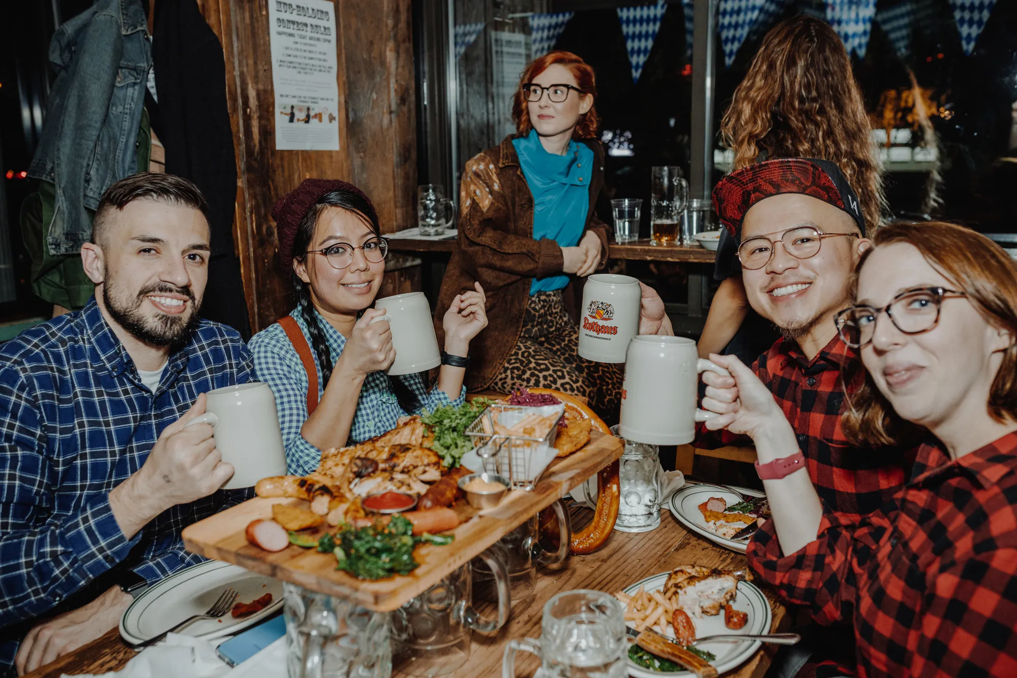 Four people hold beer steins at a table covered in seasonal foods.