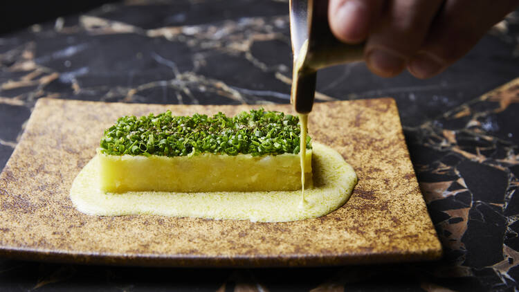 Sauce is drizzled onto a slab of fried potato topped with chives.