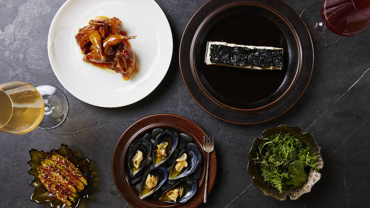 An overhead view of five dishes, including oysters and charred greens.