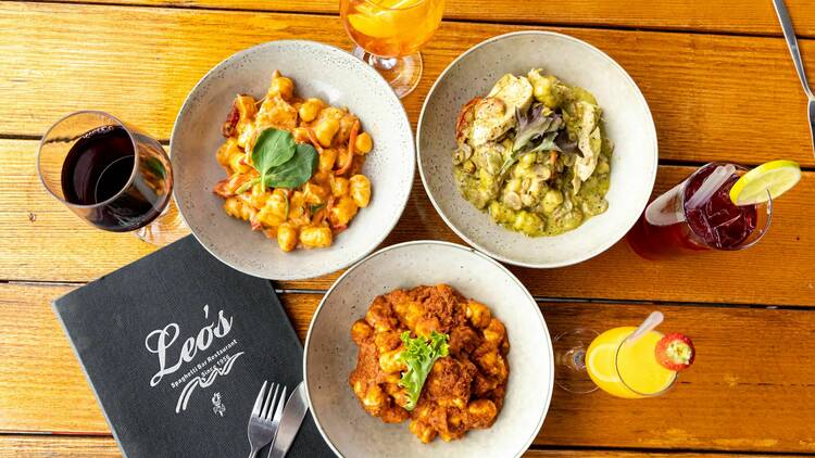 A wooden table topped with three bowls of different gnocchi styles.