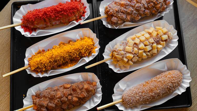 Six corn dogs coated in a variety of toppings.