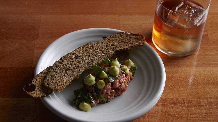 Beef tartare served with thin and crispy crackers, alongside a cocktail.