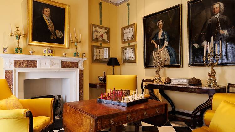 A photo of a room with historic paintings, yellow seats and a chess board 