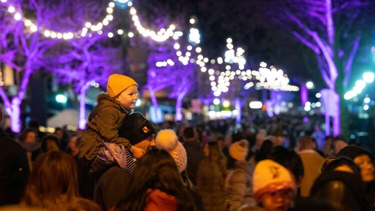 A kid is sitting on the shoulders of their dad outside at a night time light festival