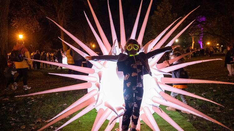 A kid stands in front of a pink and big spiky light installation