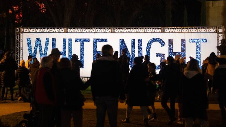 A group of people are standing in front of a sign saying 'White Night' in blue and white