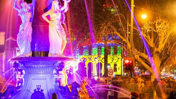 Rainbow lights are lighting up the city of Geelong and a statue at night 