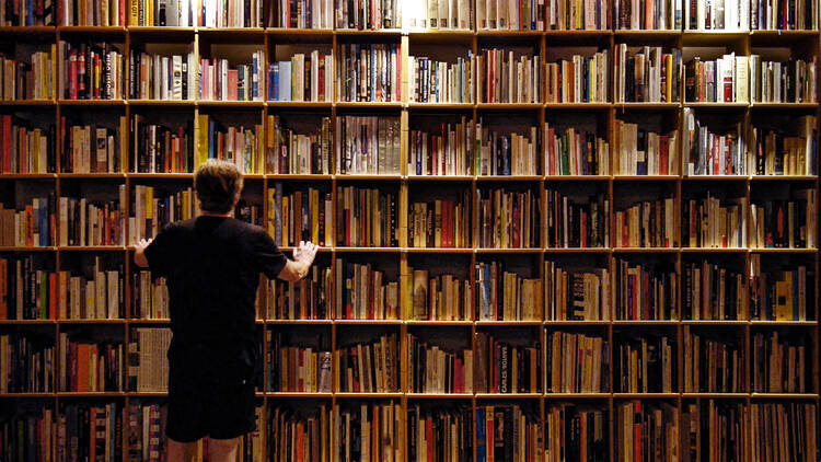 A still from the film Between the Heavens and Me, 2020. Chile. Directed by Alfredo Jaar. A person stands in front of a large shelf of books. 