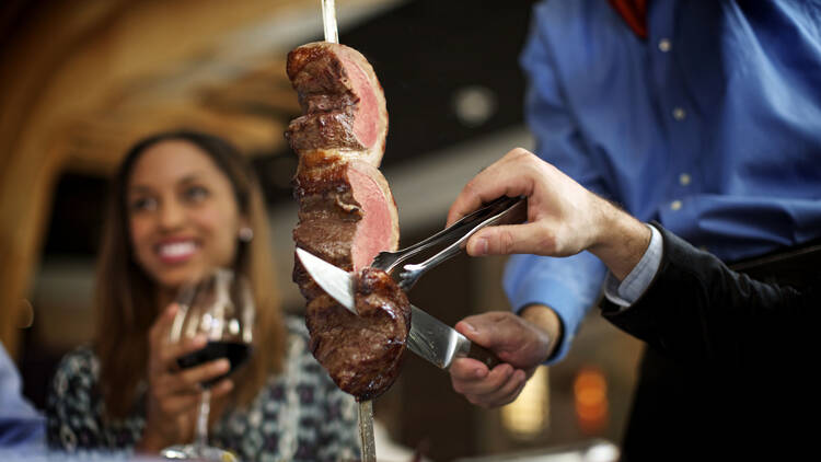 A server slicing beef on a spit onto a diner's plate.