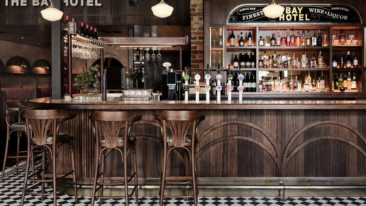 The indoor bar at The Bay Hotel with a dark wooden bar and black and white tiled floors
