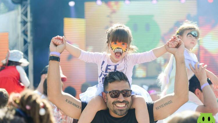 A kid sits on a man's shoulders at a rave