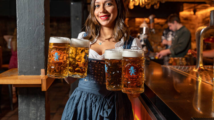 A woman dressed in an Oktoberfest outfit and holding four steins of German beer.