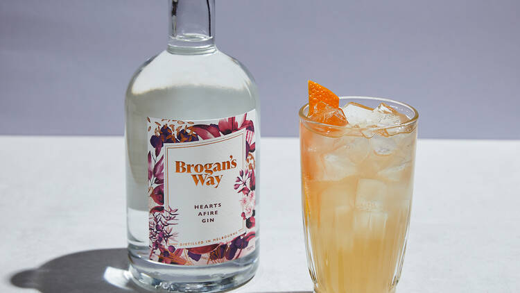 A bottle of Hearts Afire Brogan's Way gin and a glass of orange coloured gin and tonic 