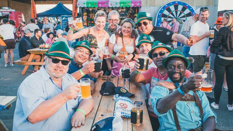 A group of people sitting at an outdoor table for an Oktoberfest celebratoin.