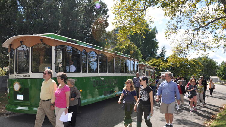 A green trolley with people walking next to it. 