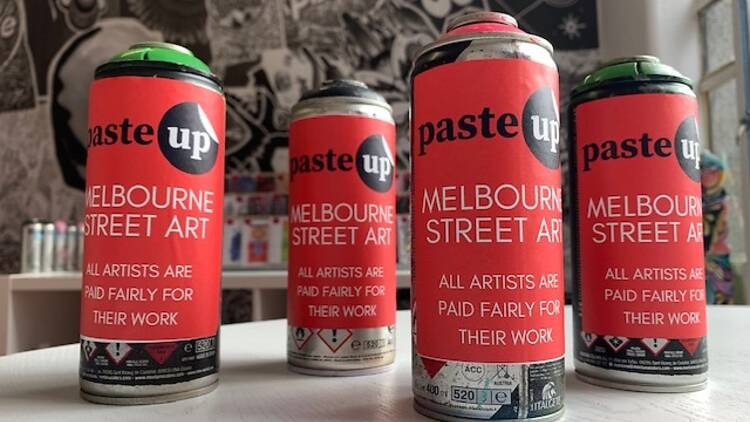 Four paint cans covered in red stickers with Pasteup branding sit upright on a table in the middle of a store.