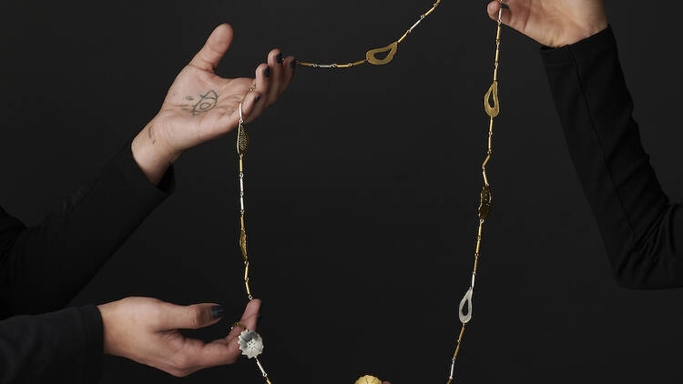 Four hands hold up a silver and gold chain necklace against a black background.