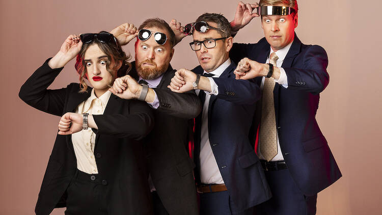 Four people in suits stand one behind another with sunglasses in their head staring at their watches.