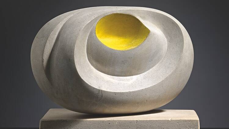 An abstract stone sculpture with a yellow spot in the centre sitting on top of a stone tile.