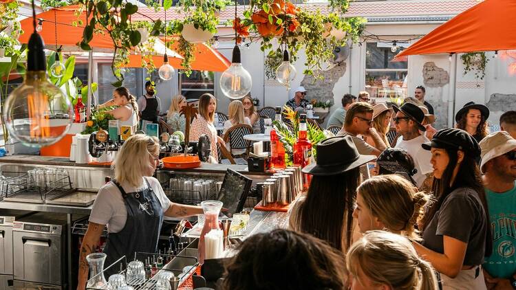 A group of people are standing and drinking at a rooftop bar