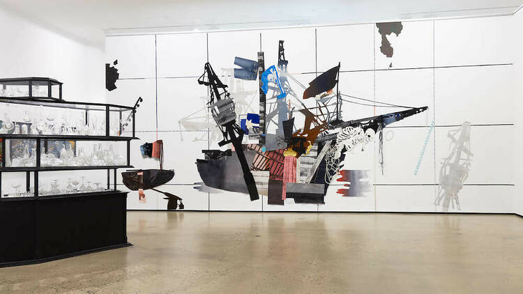 A contemporary sculpture of a pirate ship hangs from a gallery roof surrounded by other pirate paraphernalia and white walls.