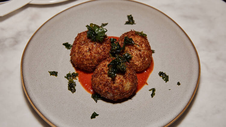 Arancini balls atop a red sauce and garnished with greens.