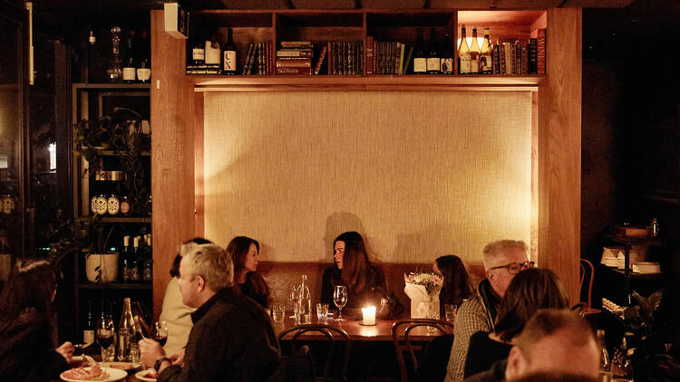 A dimly lit dining area with groups of diners seated.