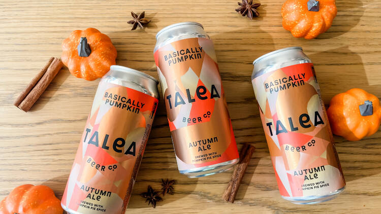 Three cans of autumn ale sit on a table next to decorative pumpkins.