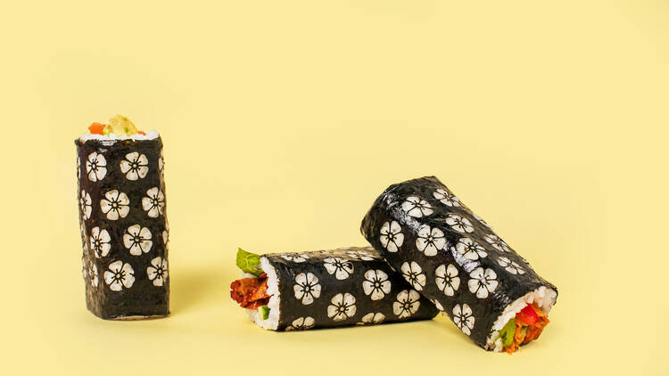Three sushi hand rolls with a flower pattern etched into the seaweed with a yellow background