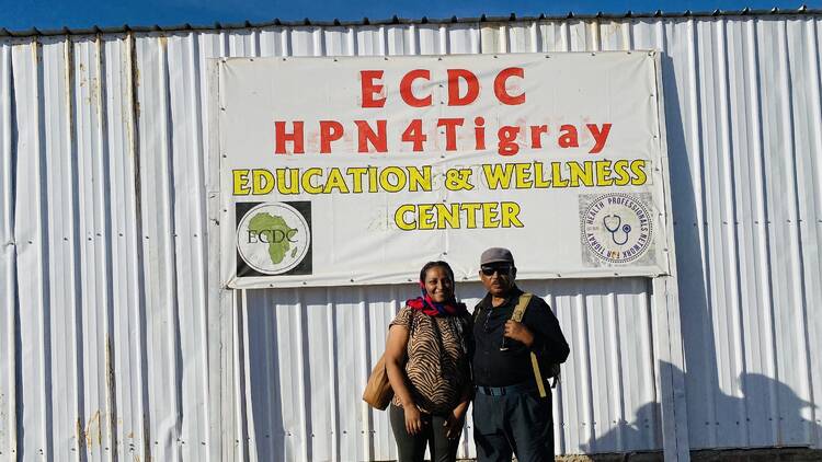 Two people stand in front of a sign that reads "ECDC HPN4Tigray"