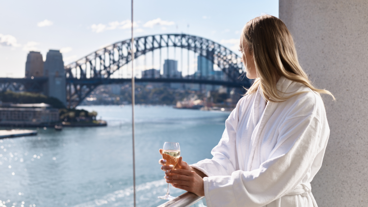 A woman stands at the balcony overlooking Sydney Harbour and the Harbour Bridge