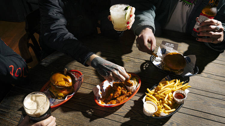A wooden table with baskets of burgers, fries and fried chicken, and different cocktails