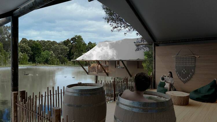 A person bathing in a hot spring barrel on a deck overlooking a lake.