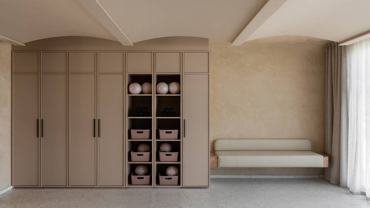 A light, modern room with seating, cupboards and shelves holding pilates equipment.