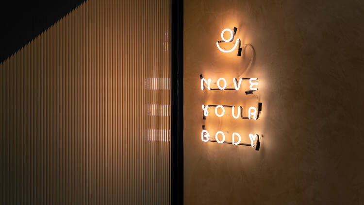 A yellow neon sign hanging on a wall that says 'move your body'.