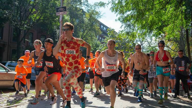 People running in a 5K with one wearing a pizza outfit.