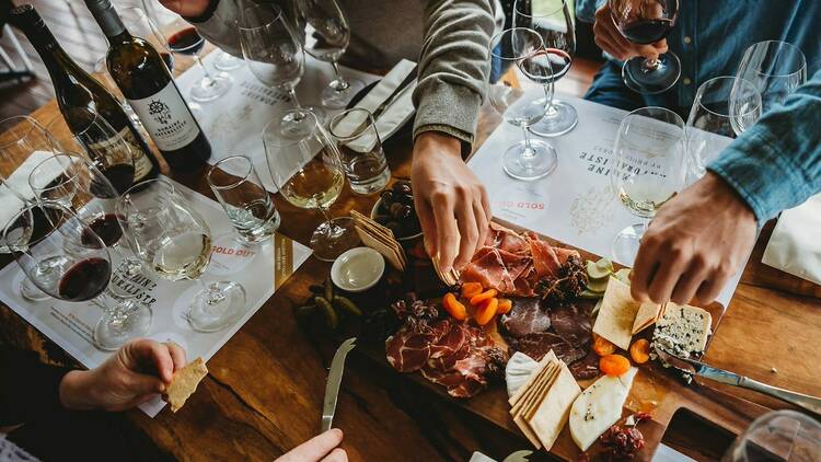 A picture of a dining experience at Domaine, a group of people enjoying wine and a charcuterie board containing crackers, cheeses, meats and apricot.